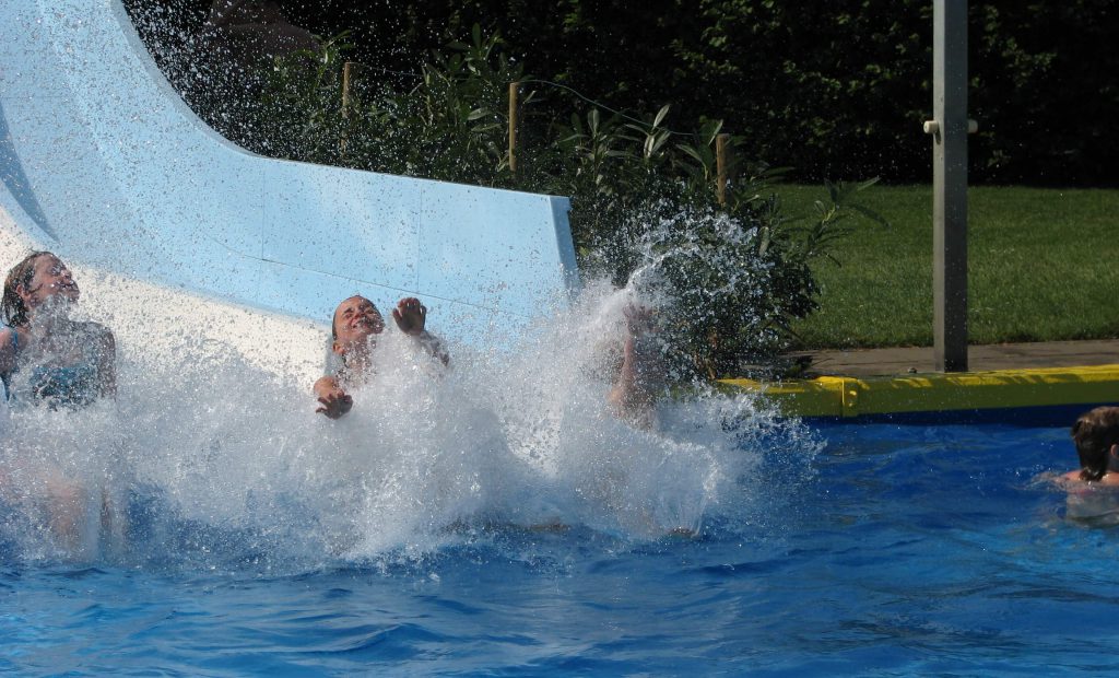 Kinderen glijden van glijbaan in zwembad met grote waterspetters en veel zwemplezier op camping