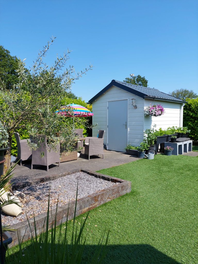 Nette campingplaats met kunstgras, tuinhuisje, terras en bloembakken op zonnige dag