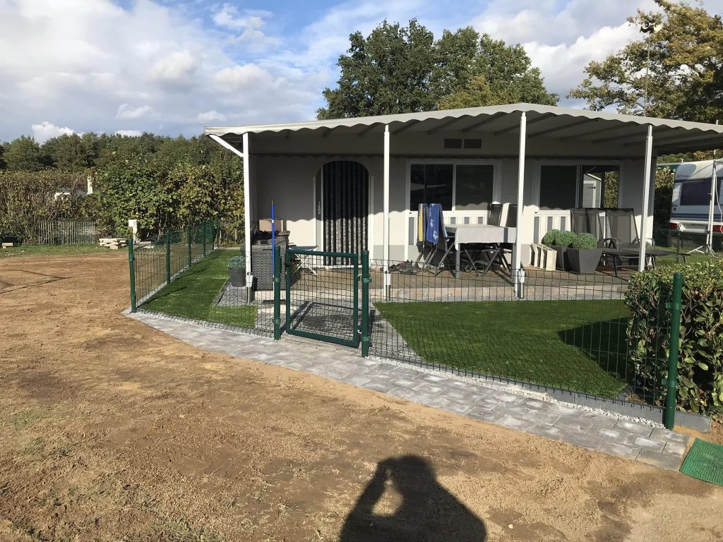 Moderne stacaravan met overdekte veranda geplaatst op camping met gravel pad en groen gazon